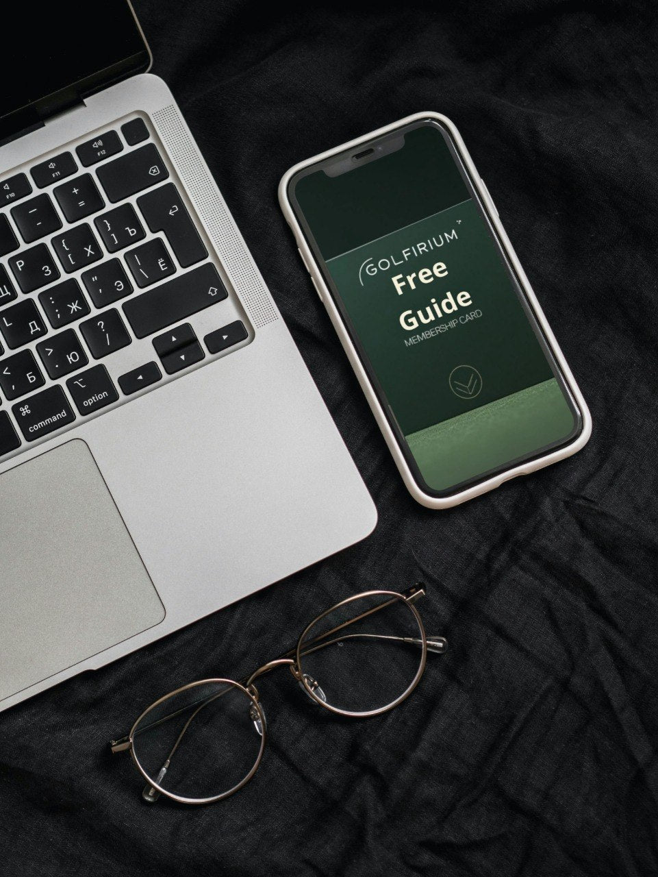 Phone displaying a Golfiriu free guide on a laptop and eyeglasses on a dark surface