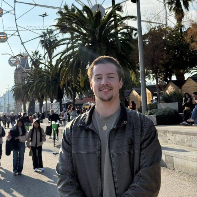 Man standing in a public area with palm trees and people in the background